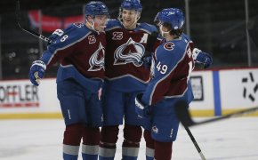 Colorado Avalanche players Cale Makar, Nathan MacKinnon, and Samuel Girard celebrating on the ice after scoring a goal during a NHL game.