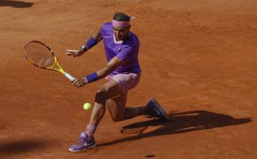 Rafael Nadal hitting a backhand return during a clay court tennis match.
