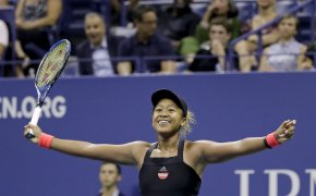 Naomi Osaka celebrating with her arms out after winning a tennis match.