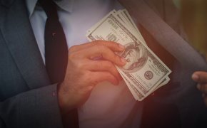 close up image of a man putting a handful of money in his suit jacket pocket