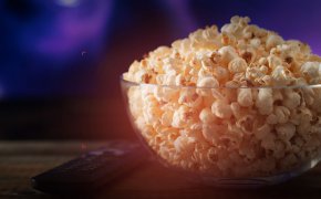 close up image of a remote and a bowl of popcorn