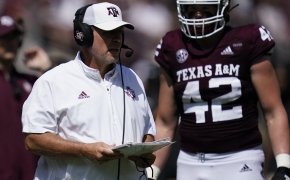 Texas A&M head coach calling a play with a player during a college football game.