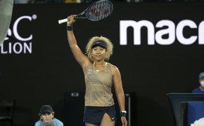 Naomi Osaka with her arm and racket in the air after winning a tennis match.