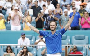 Daniil Medvedev celebrating with his hands in the air after winning a tennis match.